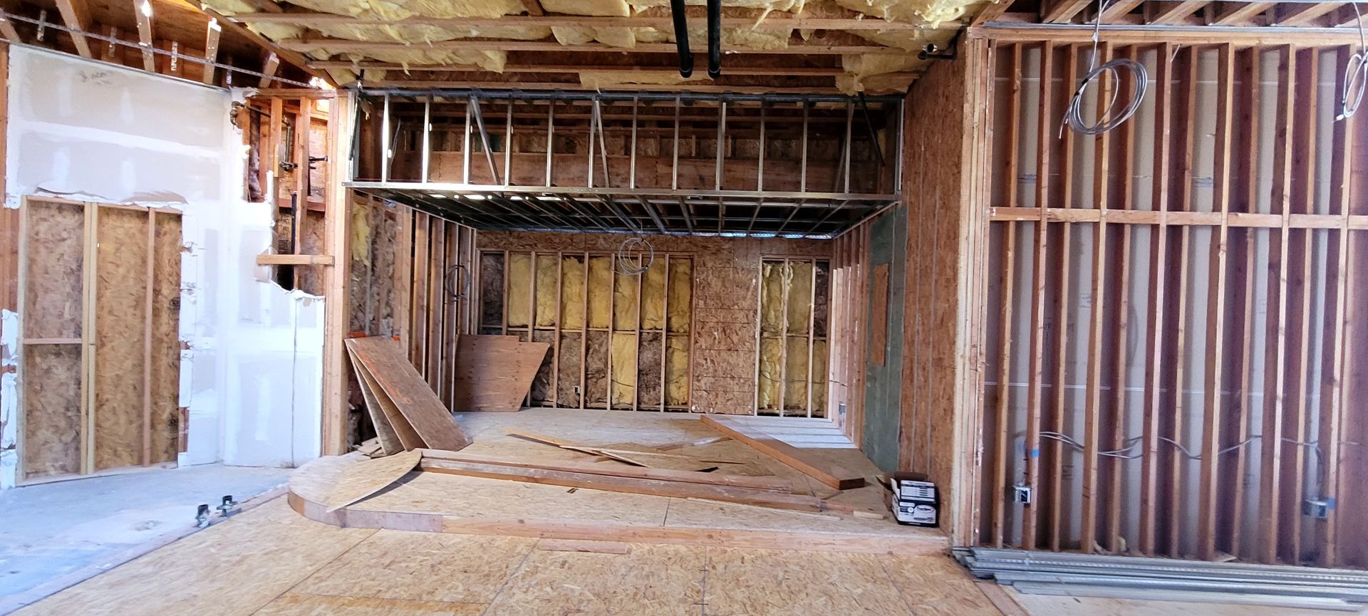 Construction site interior showing exposed wooden wall studs, insulation, and subflooring during a major renovation.