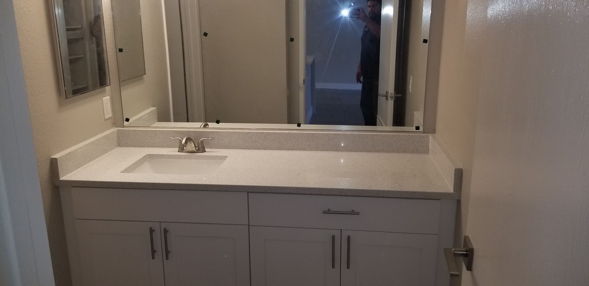 White bathroom vanity with a single sink, light stone countertop, and a wide mirror against a neutral wall.