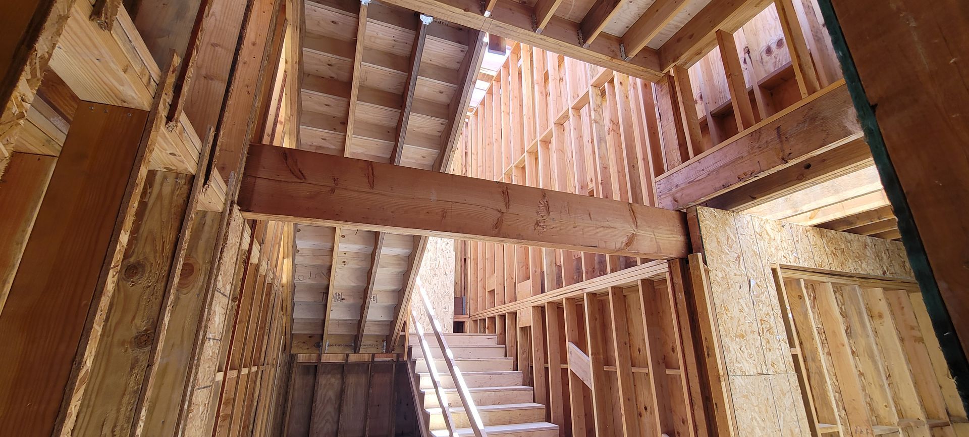 Interior construction view showing exposed wooden wall studs, floor joists, a large support beam, and a staircase.