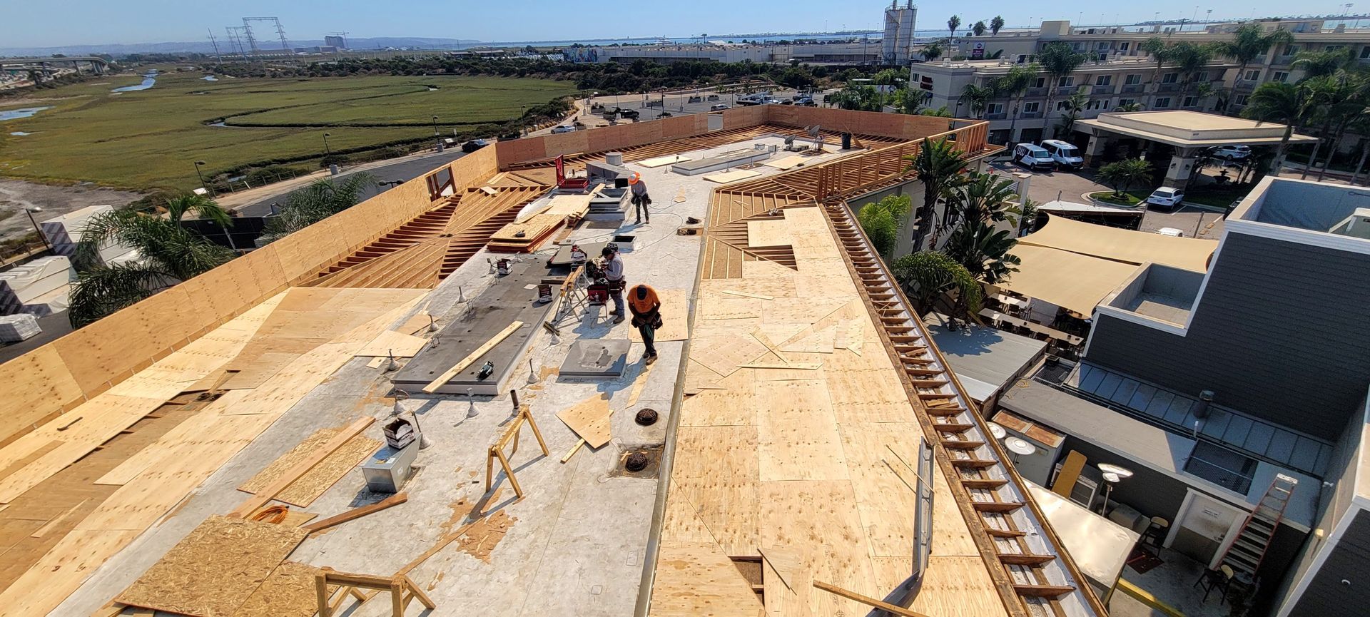 High-angle view of a construction site on a building rooftop with plywood flooring, safety barriers, and two workers.