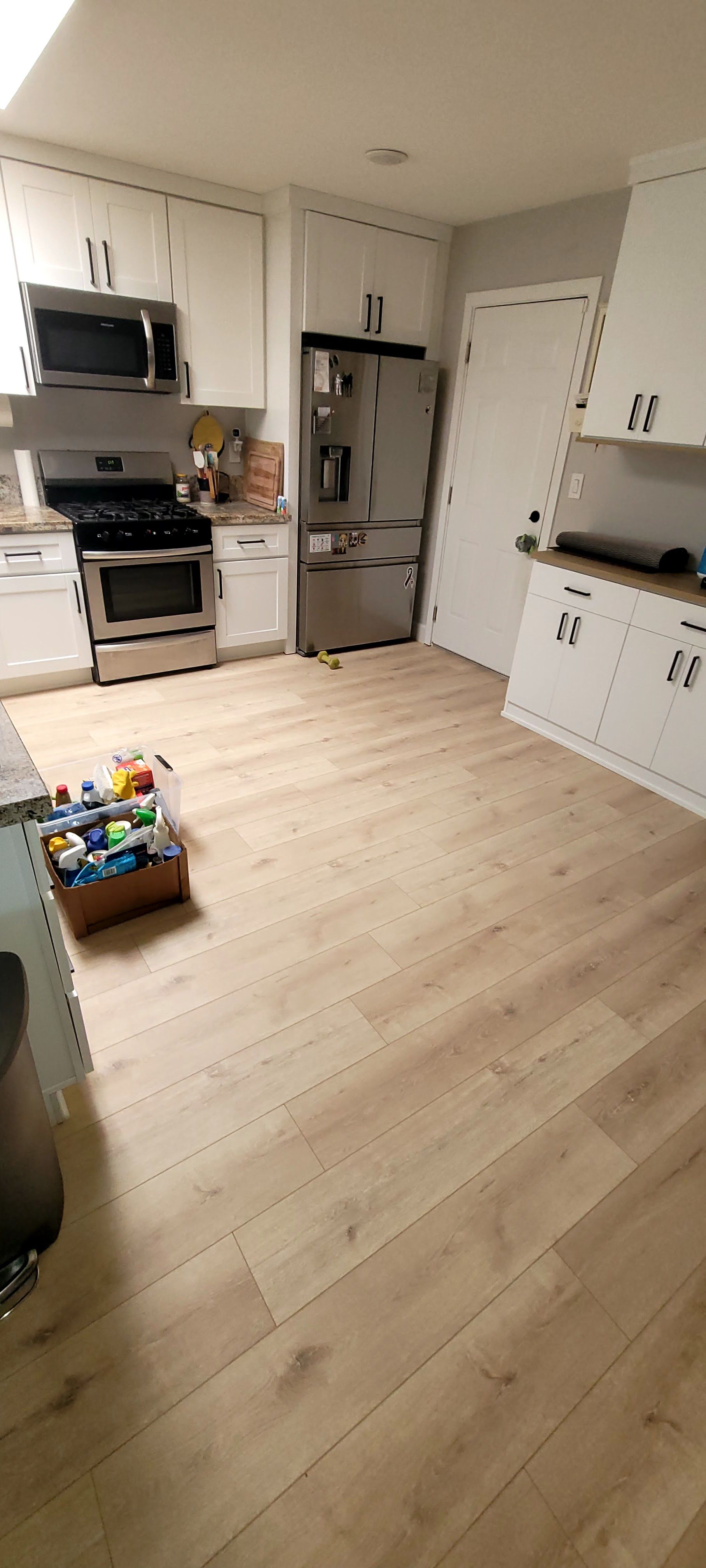 A modern kitchen with white cabinets, stainless steel appliances, and light-toned wood-look flooring.
