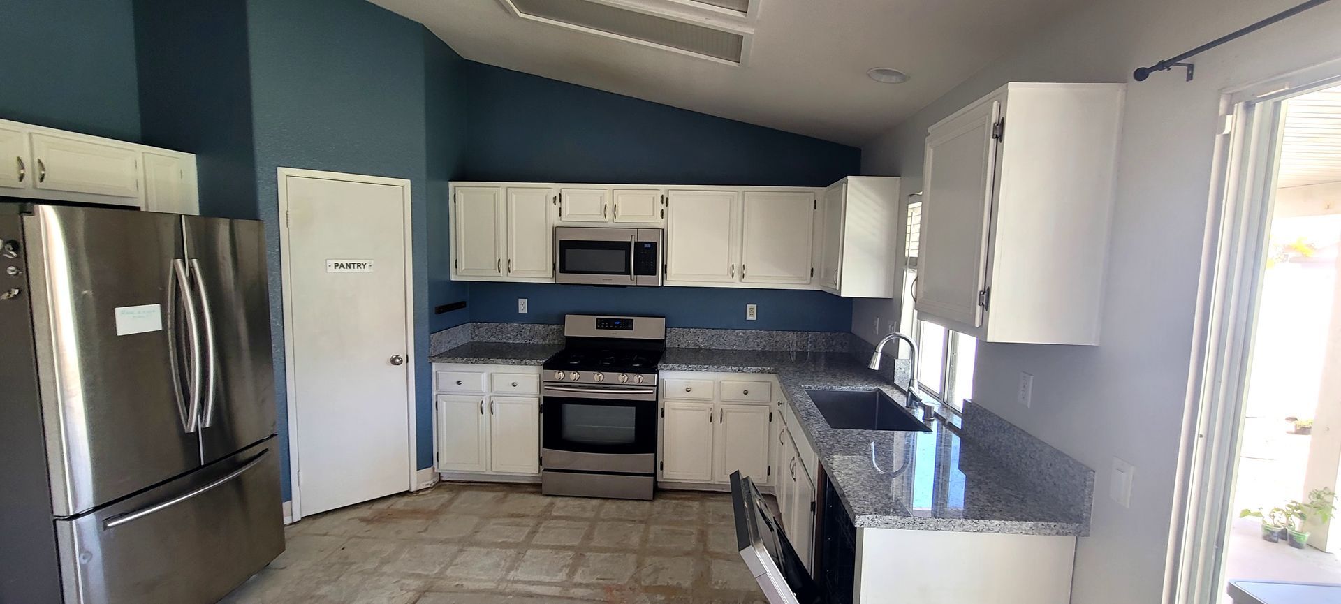 A kitchen with white cabinets, dark blue walls, stainless steel appliances, and a granite-topped peninsula.
