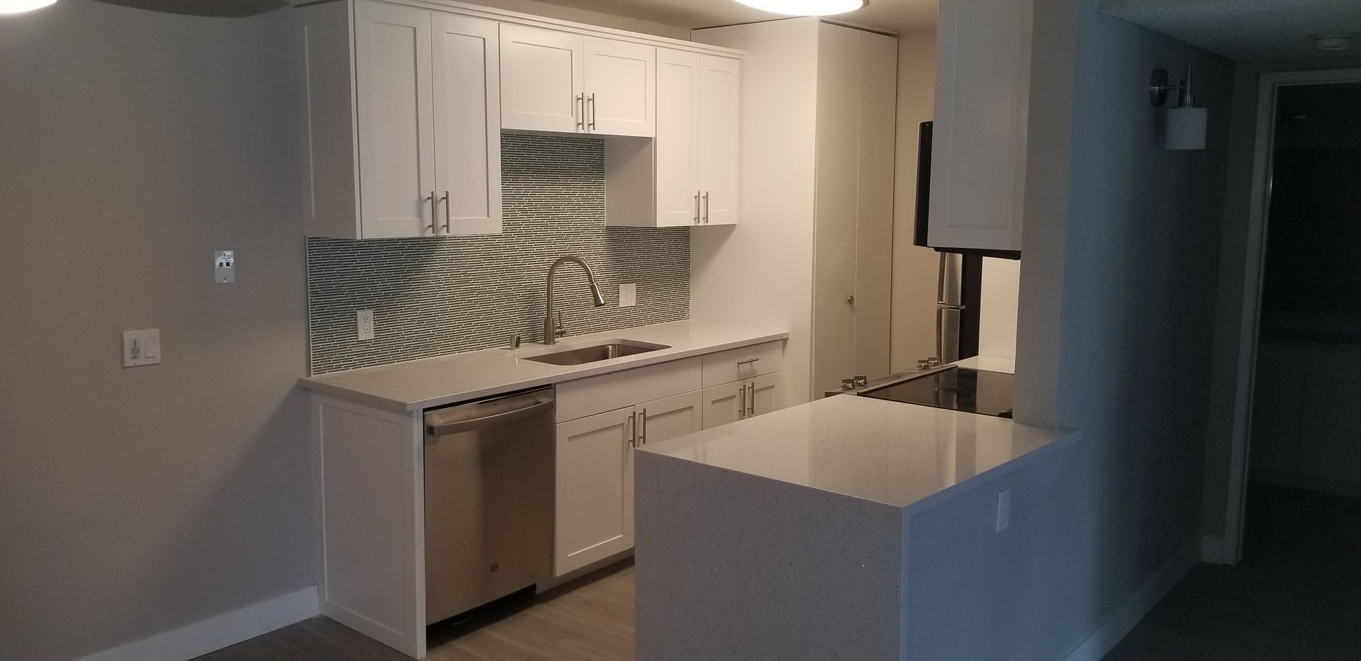 A modern kitchen features white cabinets, a light countertop, a stainless steel dishwasher, and a patterned backsplash.
