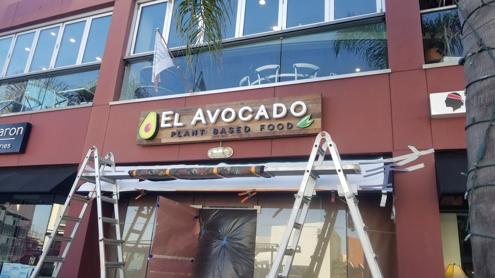 An exterior view of El Avocado, a plant-based food restaurant, with ladders positioned in front of the building's entrance.