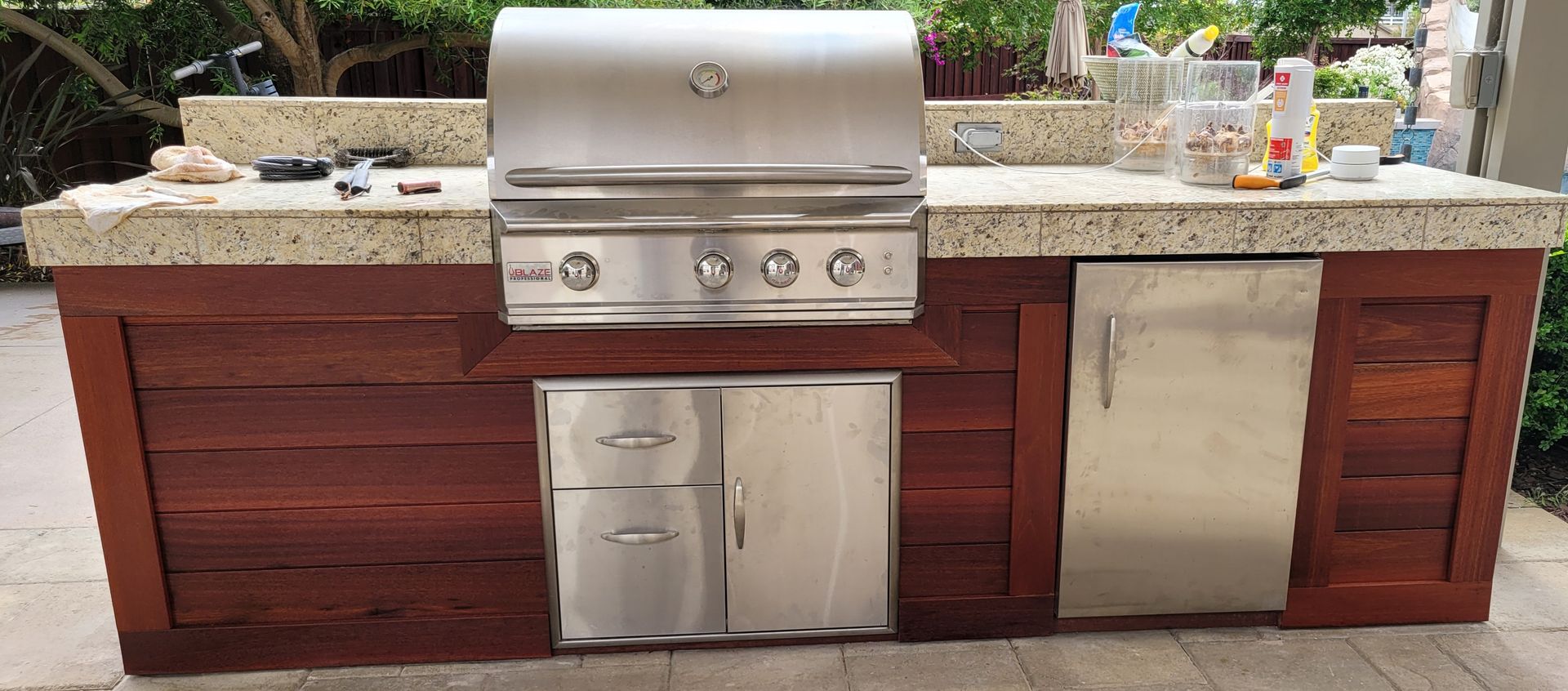 Outdoor kitchen island with a stainless steel grill, storage doors, and a stone countertop against a wooden base.