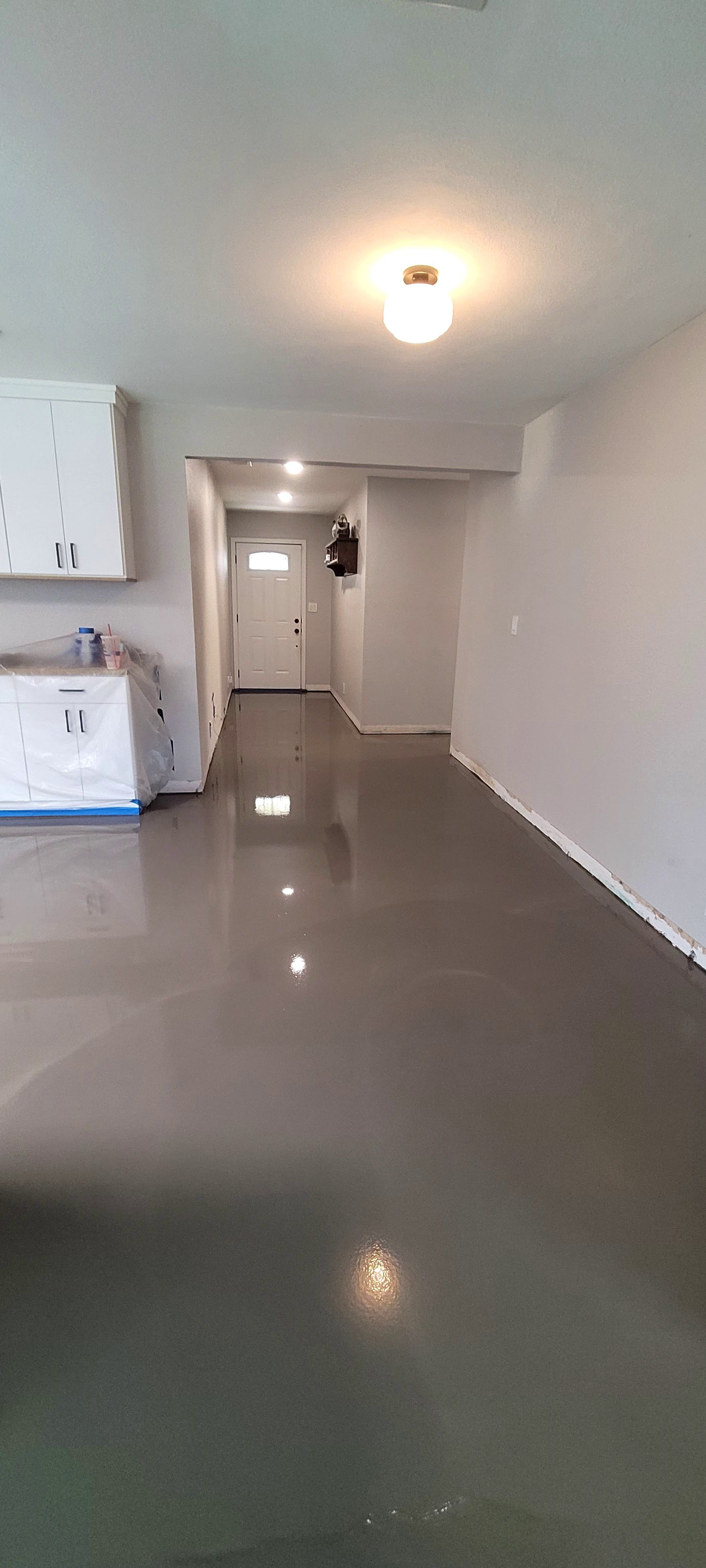 An interior view of a room with a smooth, gray epoxy-finished floor and white walls, leading toward a front entryway.