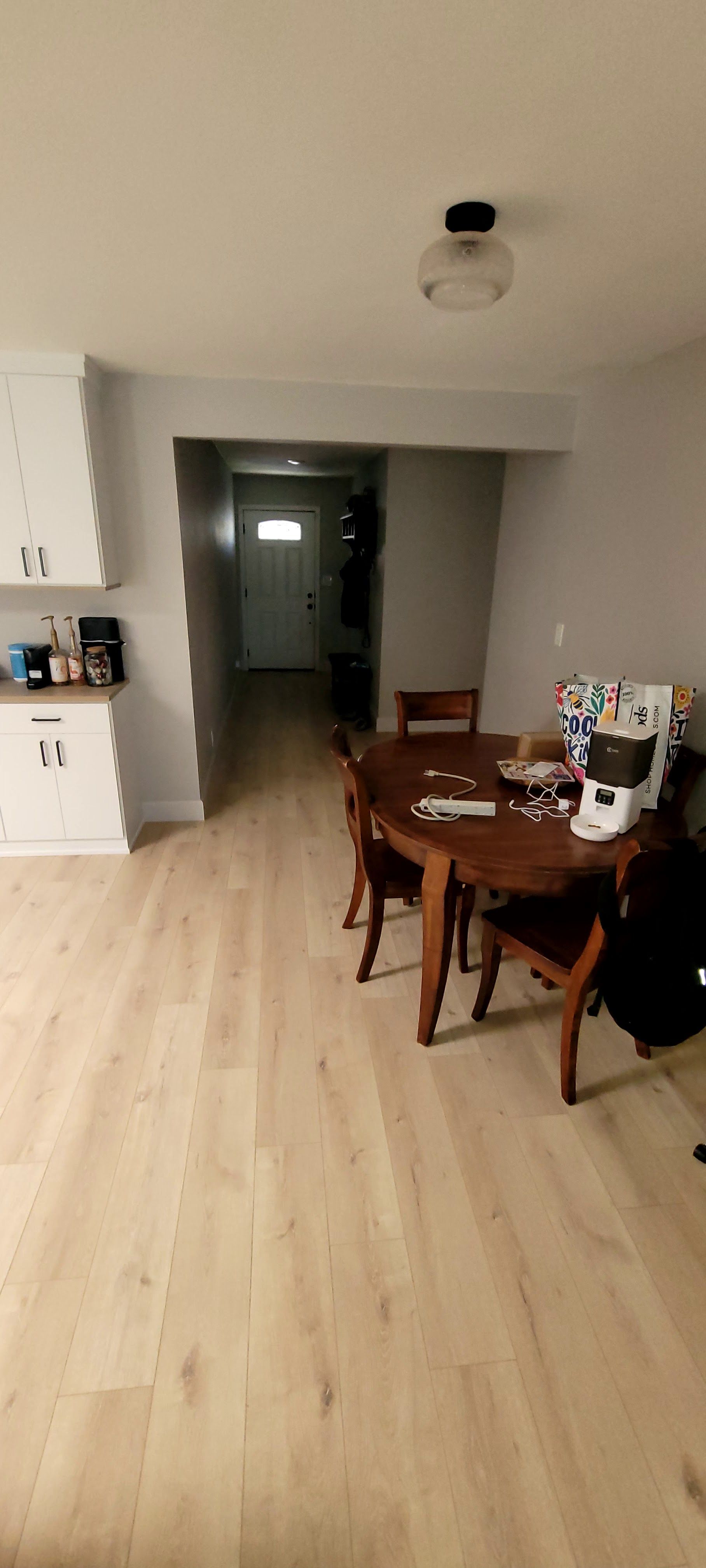 A view looking from a light wood-floored kitchen into a dining room with a round wooden table and a view of an entry door.
