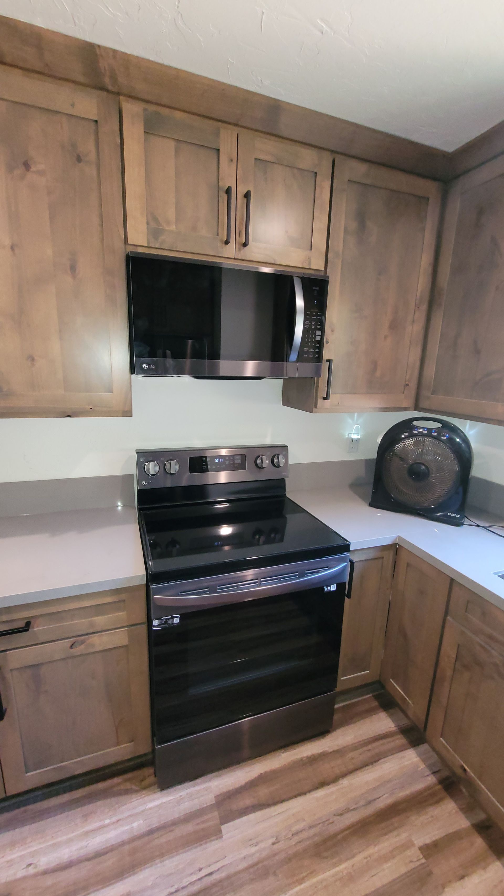 A kitchen featuring light-wood cabinets, a stainless steel stove with a matching microwave, and a black fan on the counter.