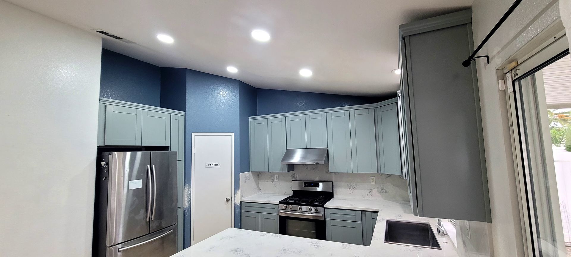 Modern kitchen with blue accent walls, light grey cabinets, stainless steel appliances, and white marble countertops.