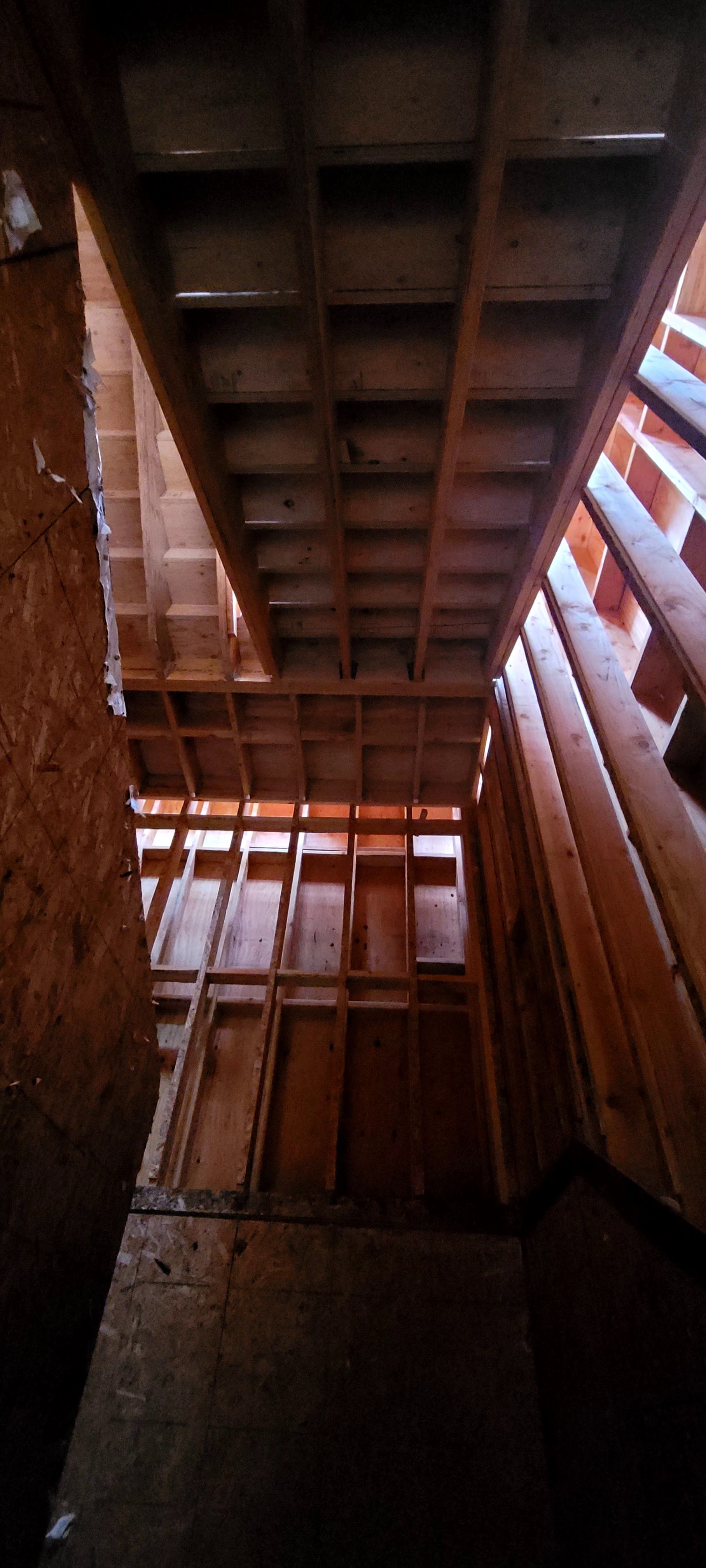 A vertical, low-angle view of wood framing for walls and floor joists in an unfinished building construction site.