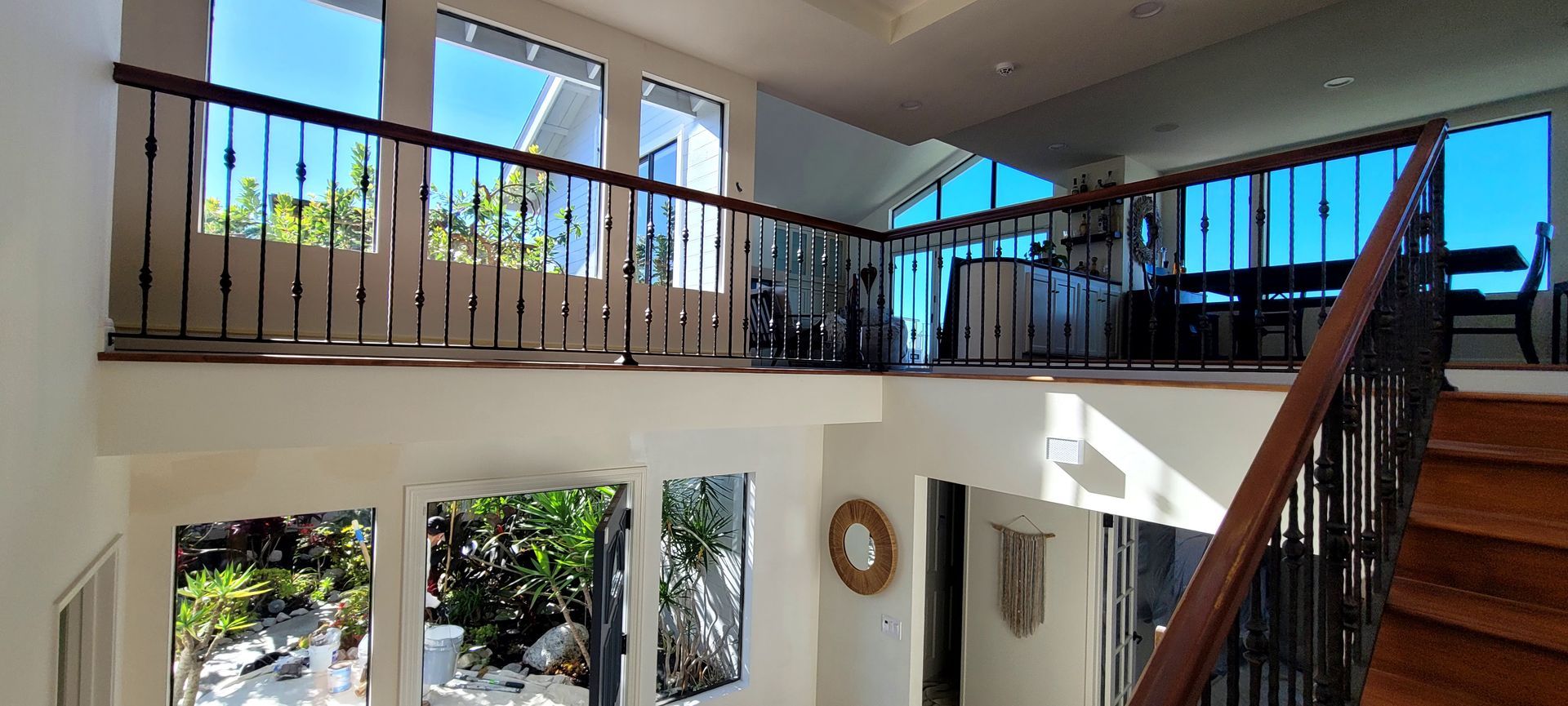A split-level interior view featuring a wooden staircase, a metal balcony railing, and large windows with garden views.