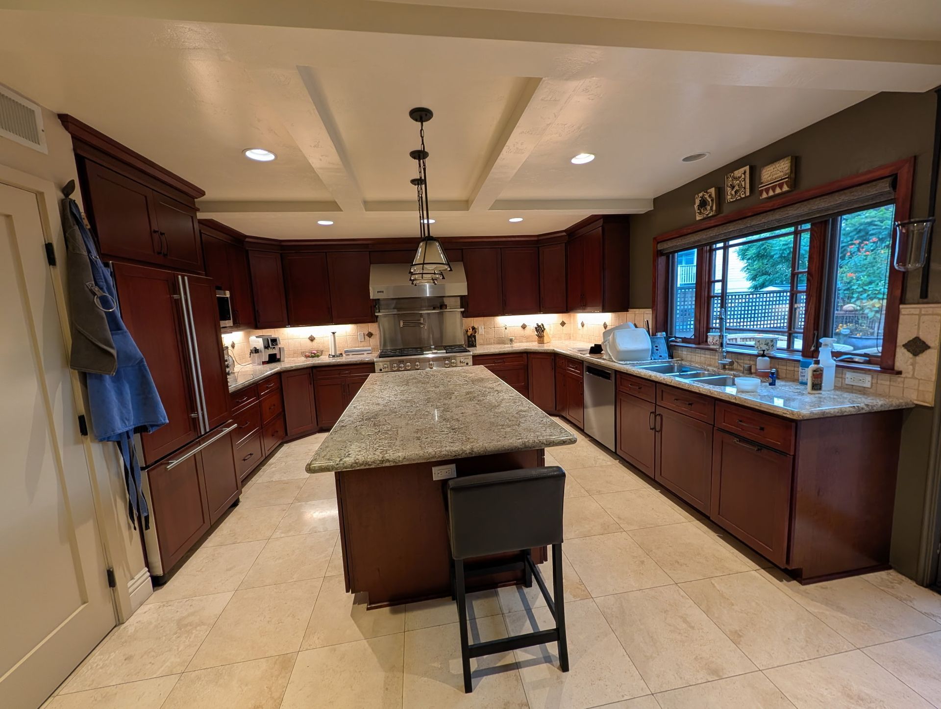 Spacious kitchen with dark wood cabinets, a granite island, a single stool, and a large window above the sink.