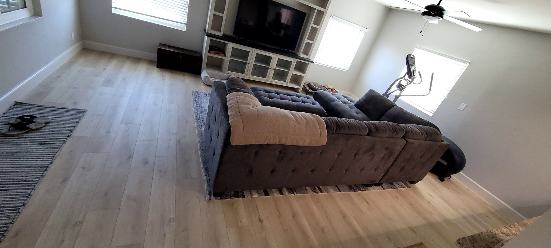A wide-angle interior view of a living room with light wood floors, a large grey sectional sofa, and a media console.