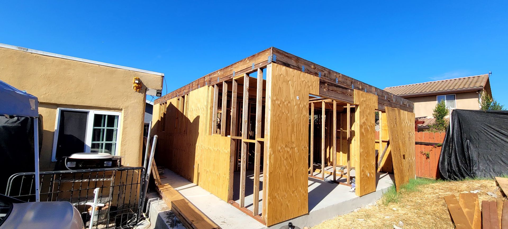 A construction site showing the wooden frame and plywood sheathing of an addition being built onto a house.
