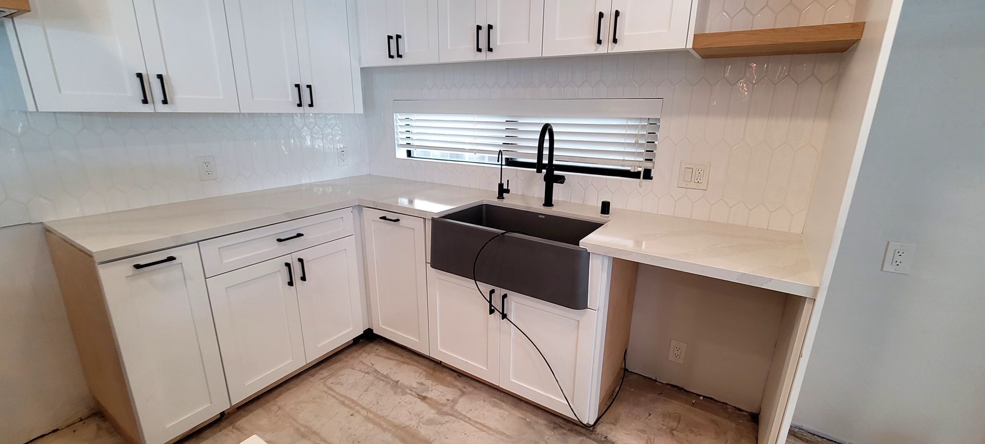A kitchen with white cabinets, a dark farmhouse sink, a black faucet, and a light-colored countertop.