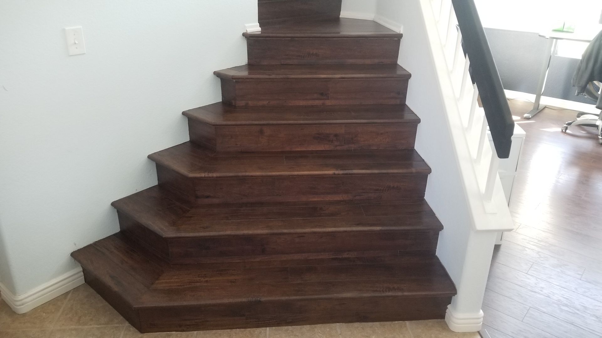 A set of dark-stained wooden stairs with angular, winding treads in a home with white walls and a white banister.