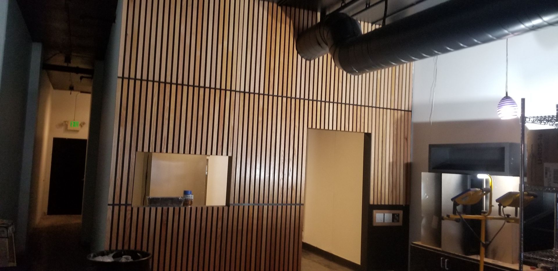 A high, decorative wooden slat wall features vertical lines and two rectangular openings in an interior space.