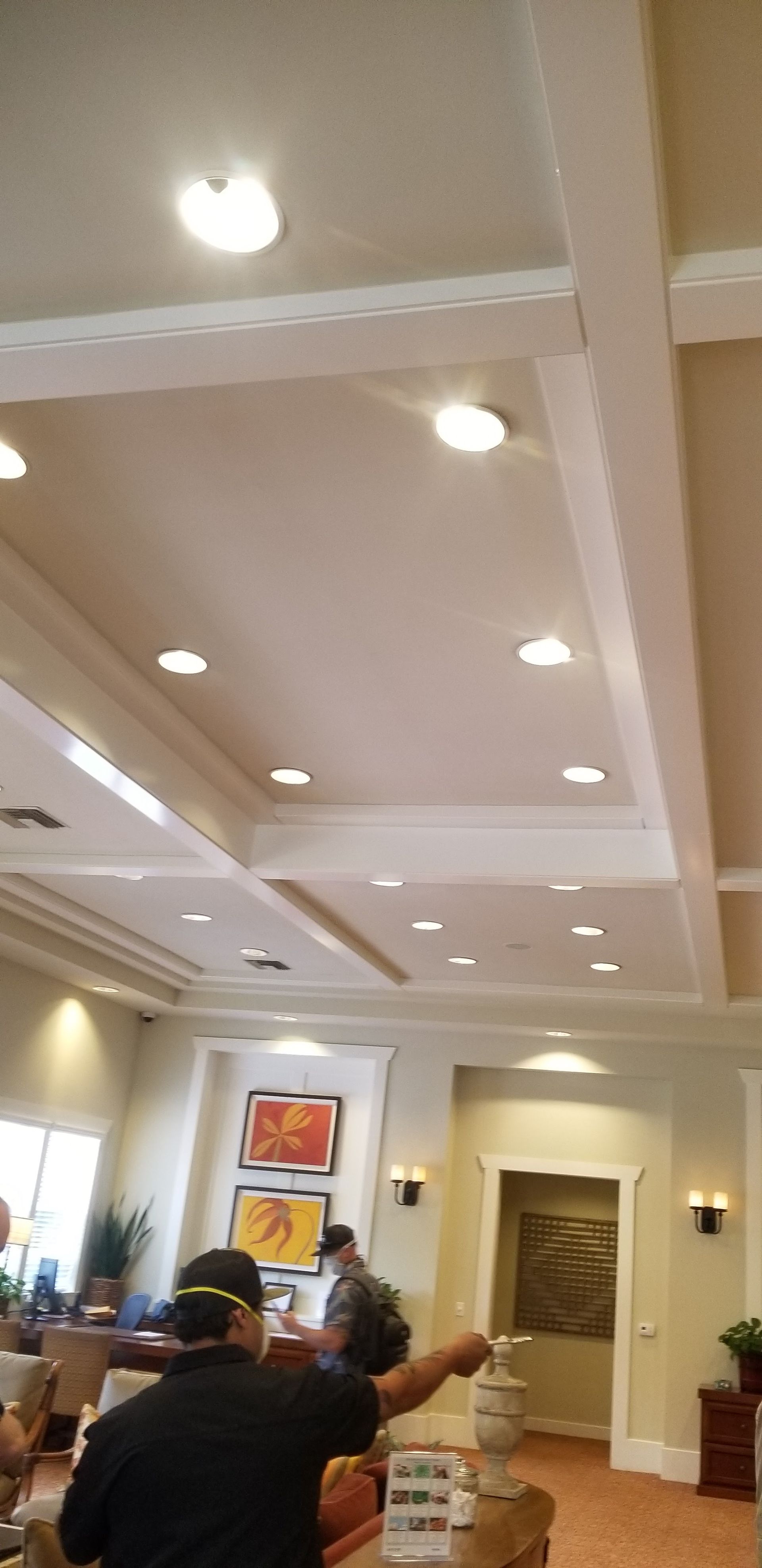 An interior view of a lobby with a coffered ceiling, recessed lighting, and a person standing at a reception desk.