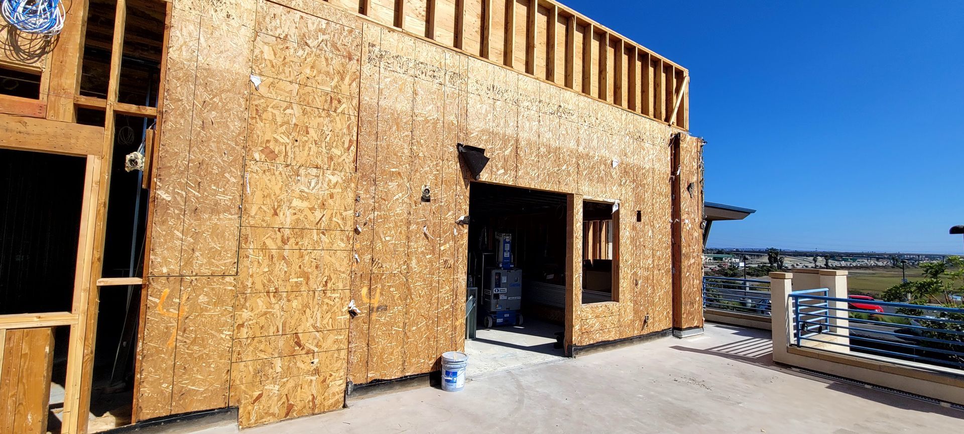 Construction site with a plywood-sheathed building frame on an outdoor deck overlooking a scenic landscape.