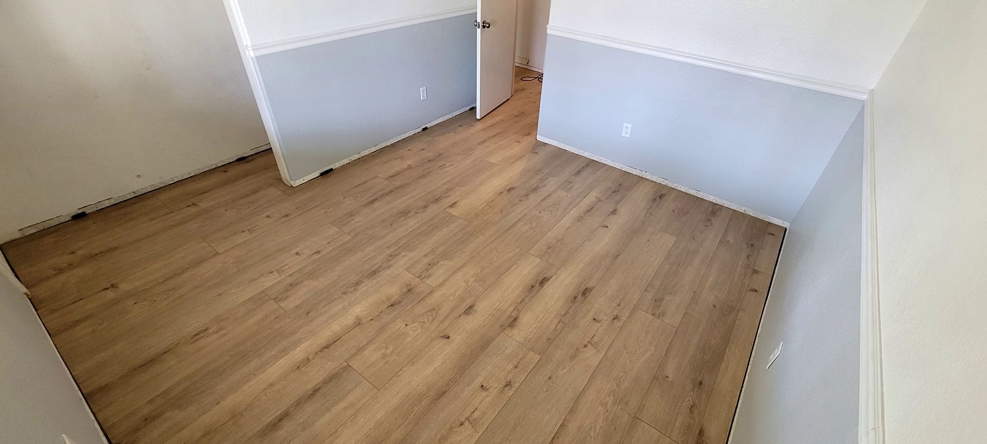 Empty room with light wood-look flooring and walls painted white on top and light blue on the bottom.
