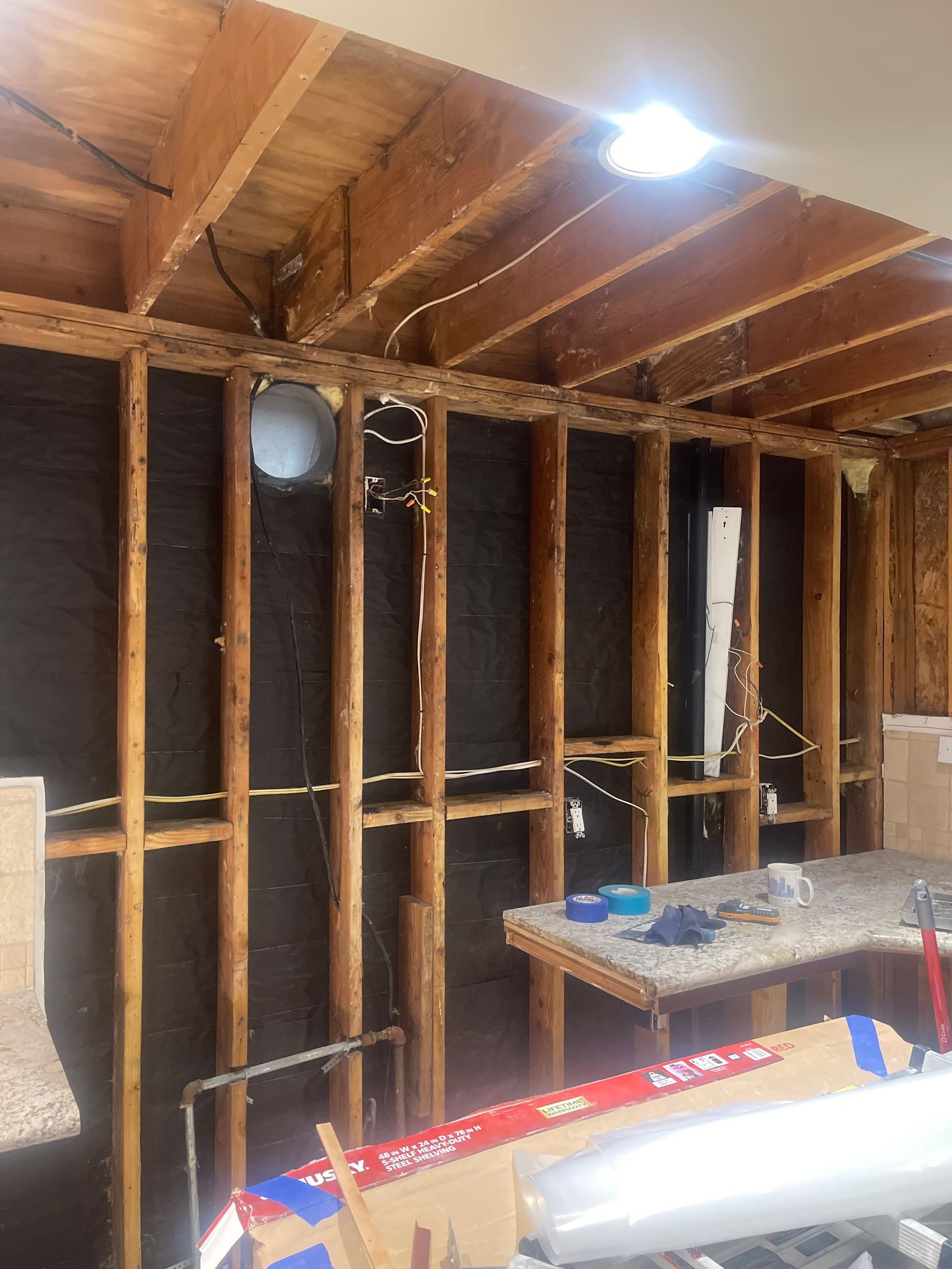 Exposed wooden wall studs and ceiling joists in a room under construction, with dark insulation and exposed wiring.