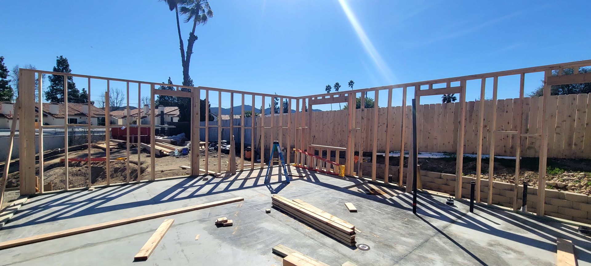 Wood frame walls under construction on a concrete foundation under a bright blue sky.