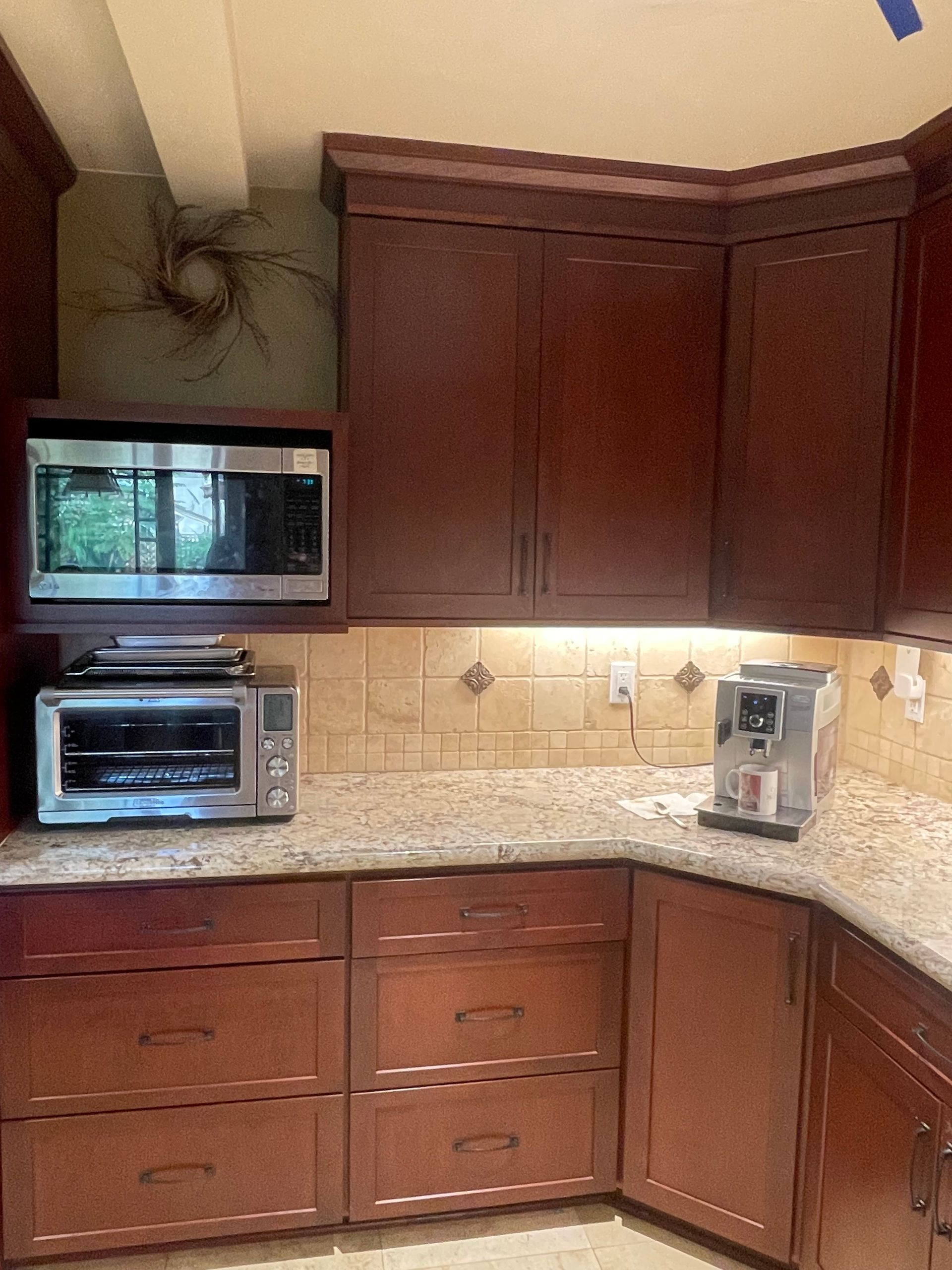 A kitchen corner with dark wood cabinets, a built-in microwave, a toaster oven, a coffee maker, and speckled countertops.