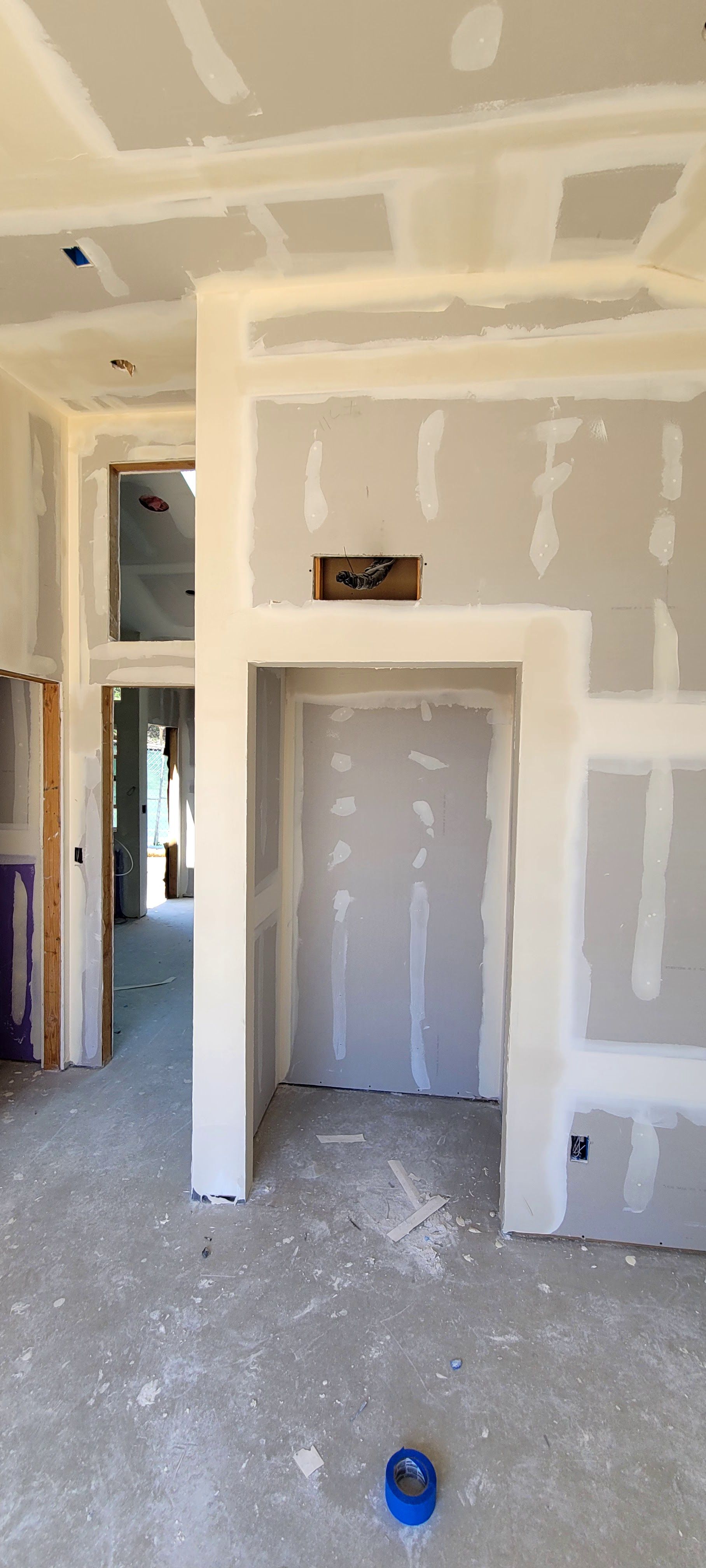 A construction site interior showing framed doorways and ceilings with partially finished, taped drywall.