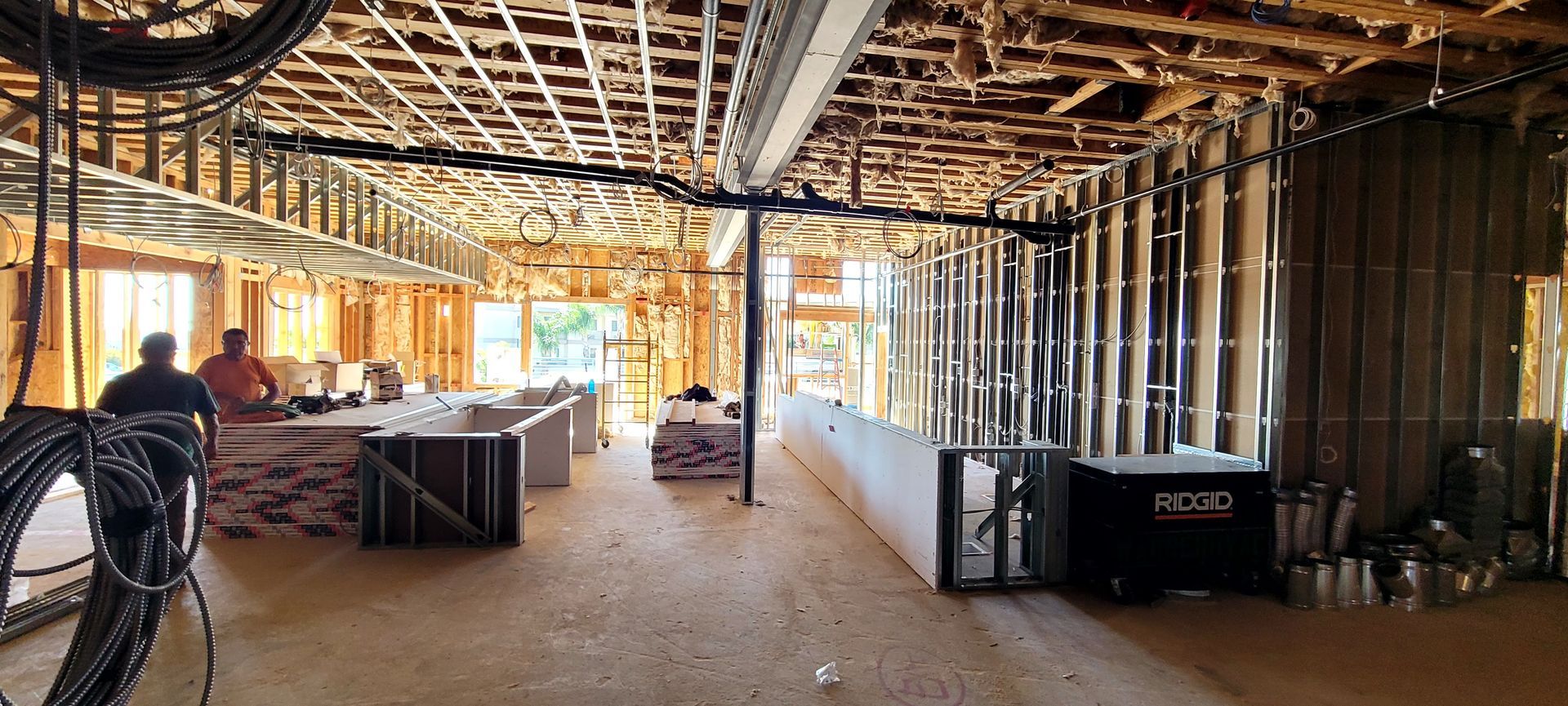 Interior construction site with wooden framing, metal studs, unfinished ceilings, and workers in a large open space.