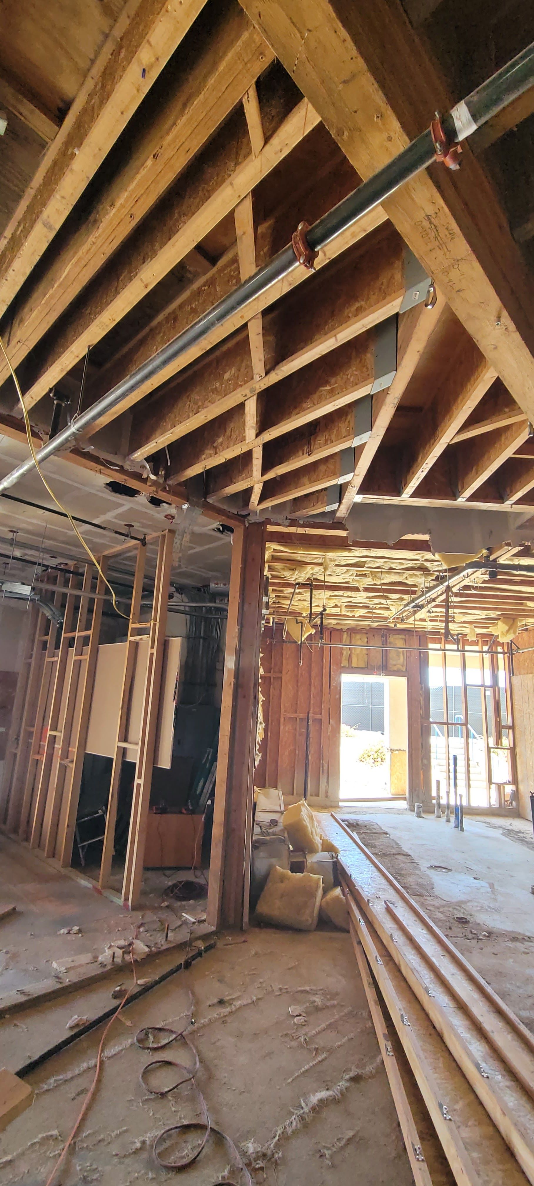 Interior view of a building under renovation with exposed wooden ceiling joists, wall framing, and construction debris.