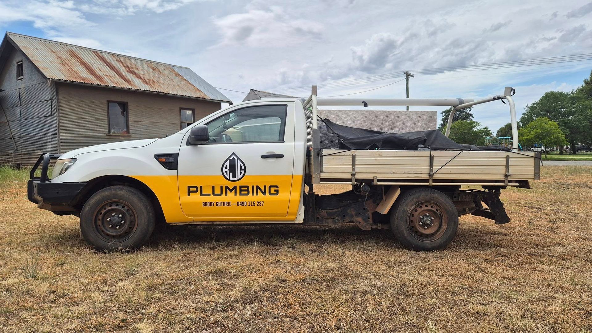 White and yellow plumbing service truck with a toolbox parked outside a barn — BJG Plumbing in Coolamon, NSW