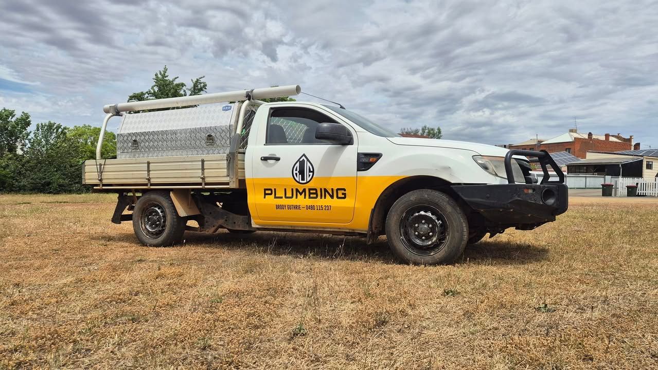 White and yellow plumbing service truck parked on dry grass field under cloudy sky — BJG Plumbing in Coolamon, NSW