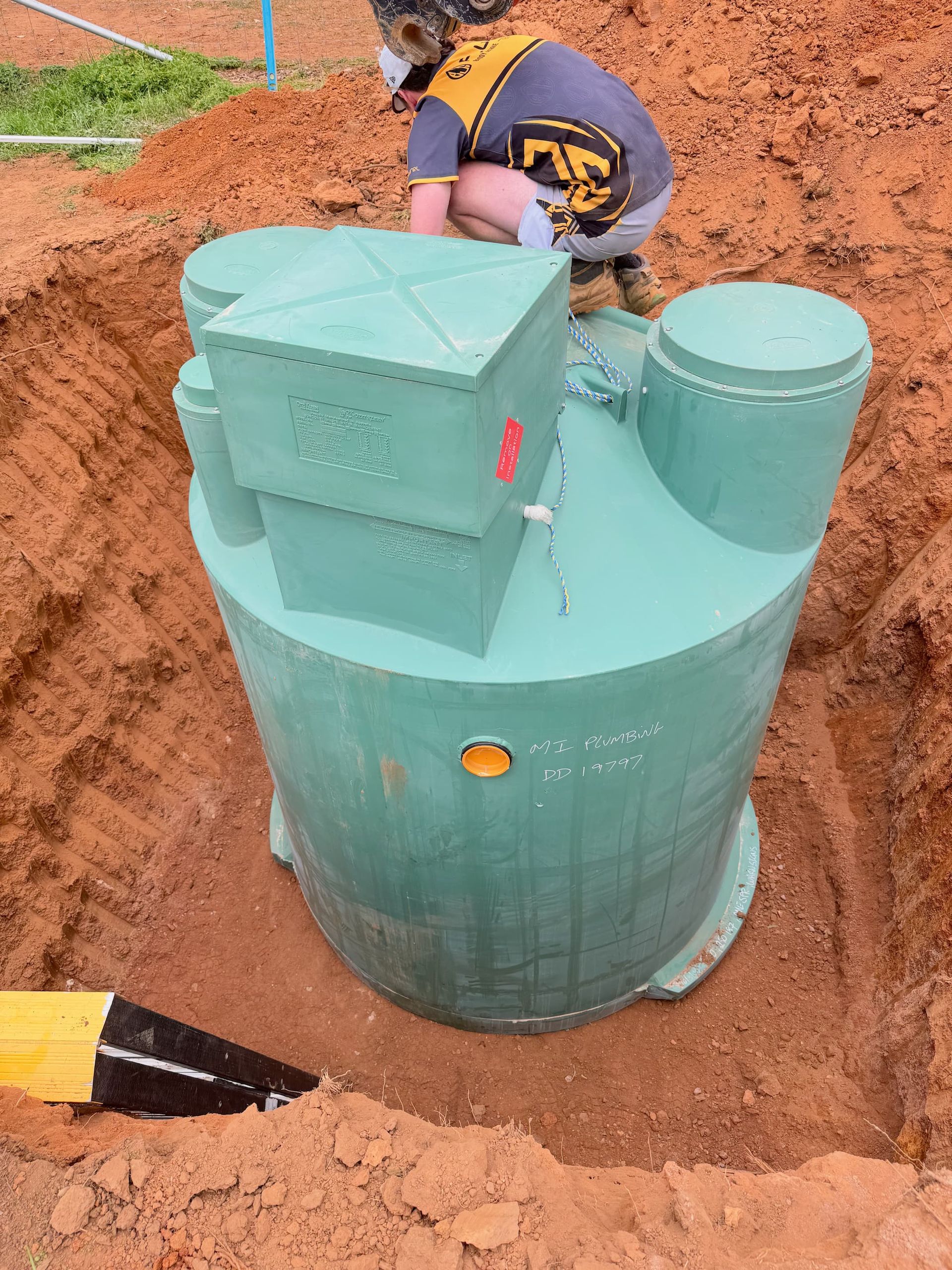 Man installing a large green septic tank in a dirt trench — BJG Plumbing in Coolamon, NSW