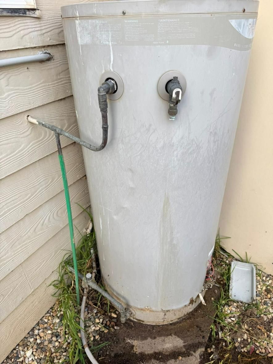 Large Gray Water Heater Tank Outdoors Near Building Siding With Green Hose Attached — BJG Plumbing in Coolamon, NSW