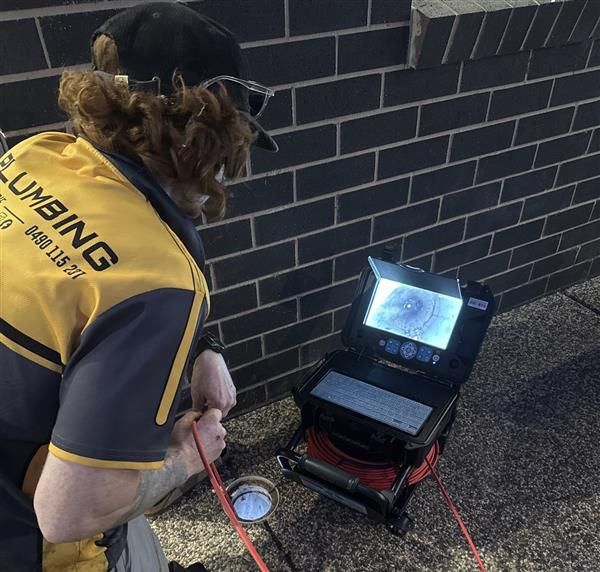 Plumber using a camera to inspect a drain outside a brick building — BJG Plumbing in Coolamon, NSW