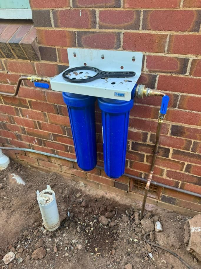 Blue Water Filter System Mounted On Brick Wall Above Dirt — BJG Plumbing in Coolamon, NSW