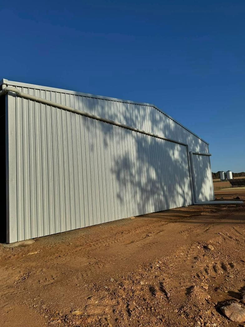 White Corrugated Metal Shed Under Clear Blue Sky Casting Shadows On Dry Brown Ground — BJG Plumbing in Coolamon, NSW