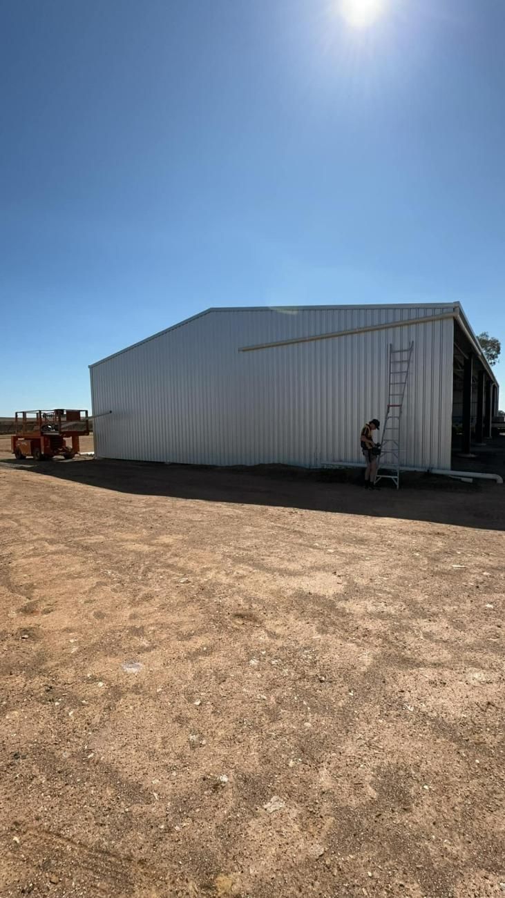 Metal Barn On Dirt Lot Under Bright Blue Sky With Person Near Entrance — BJG Plumbing in Coolamon, NSW