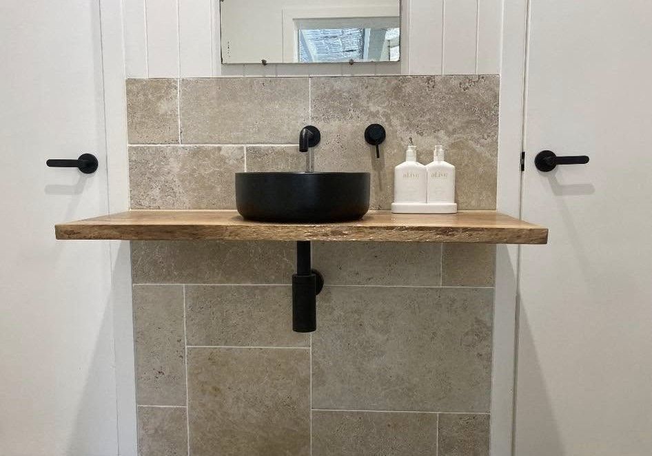 Black Sink on A Wooden Shelf Against a Stone Wall, Flanked by White Doors with Black Handles — BJG Plumbing in Coolamon, NSW
