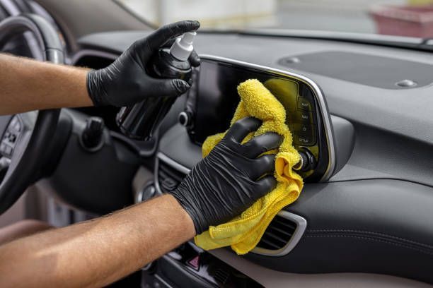 A person wearing black gloves is cleaning the dashboard of a car.