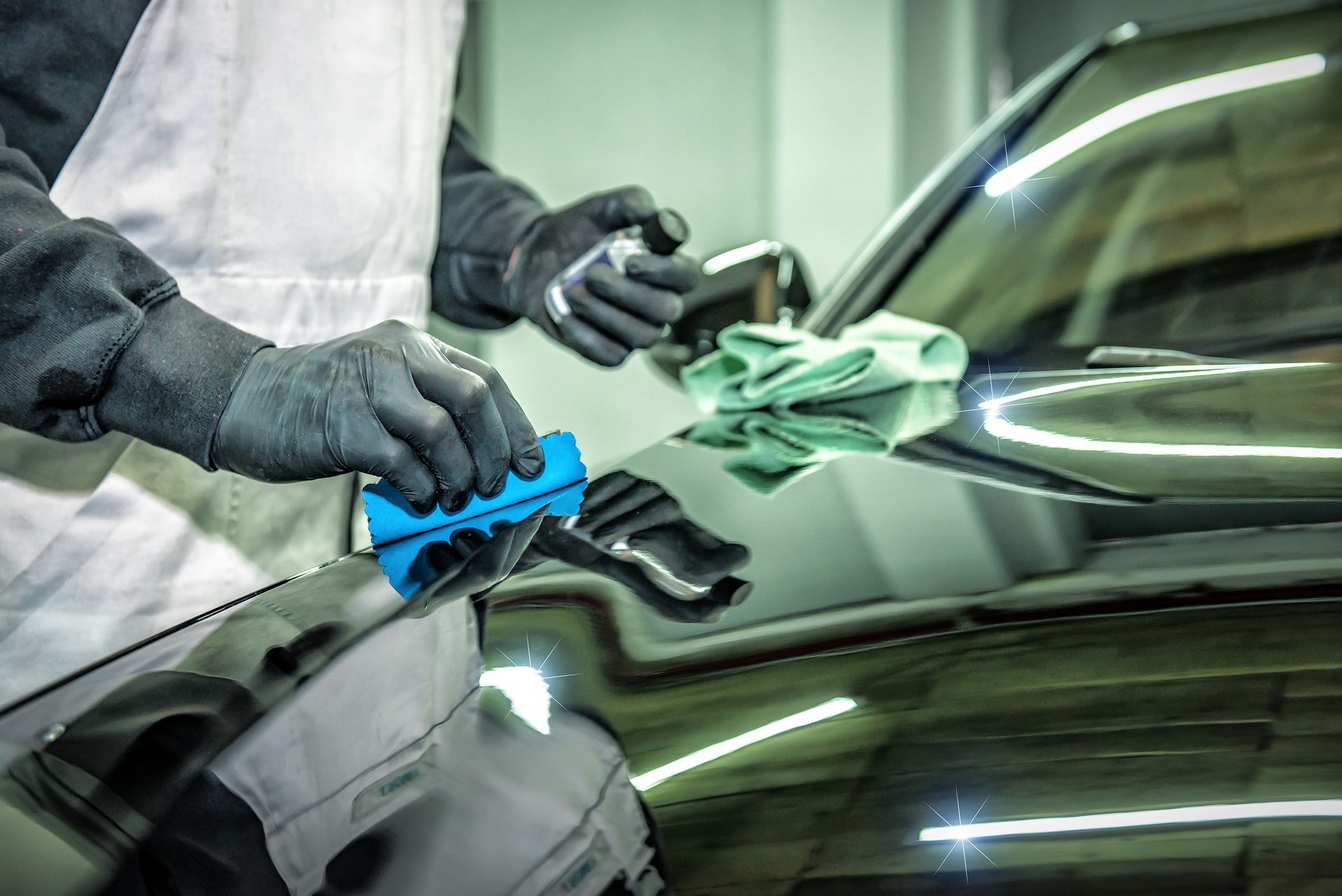 A man is polishing the hood of a car with a blue sponge.