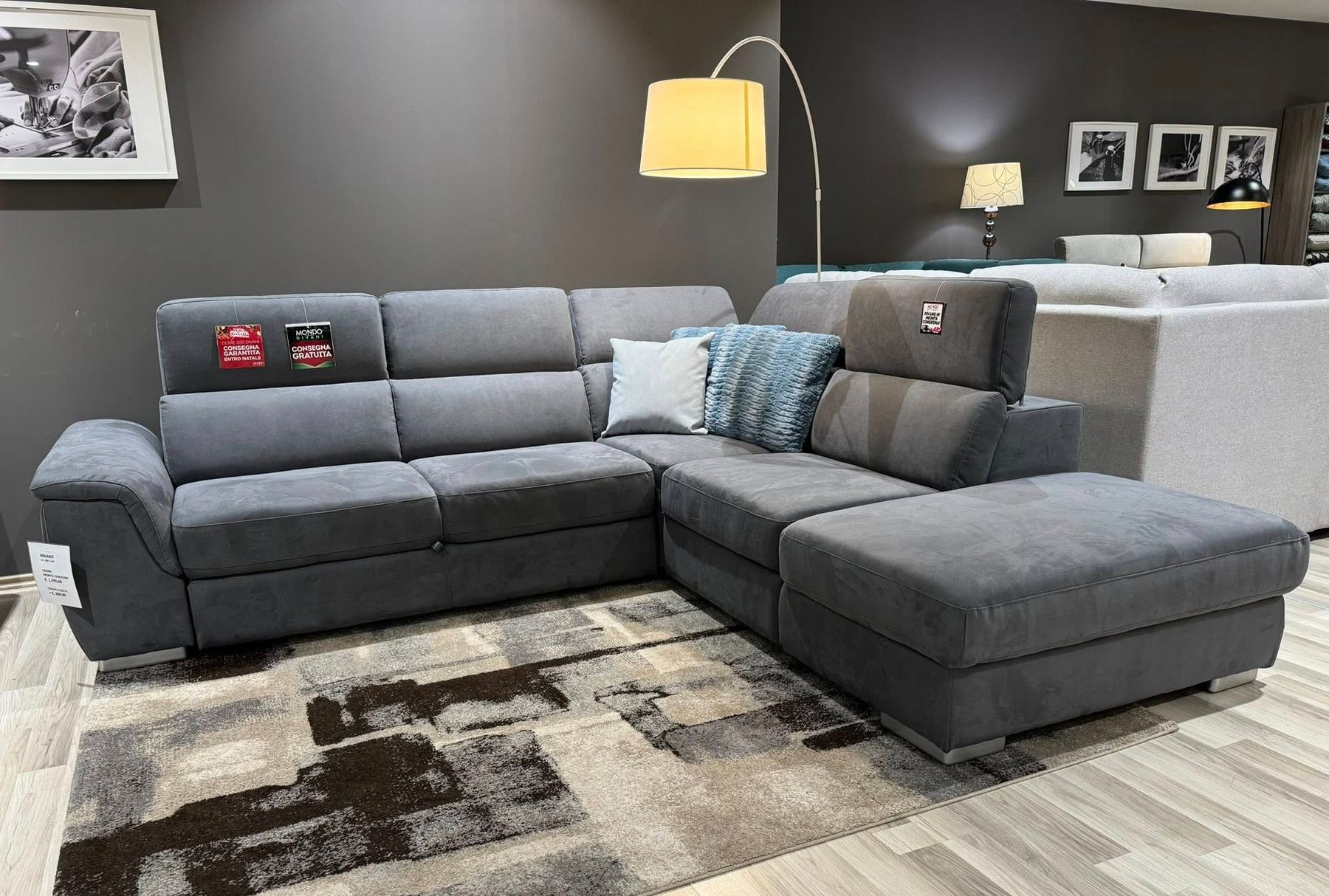 Divano componibile grigio con chaise longue su un tappeto a fantasia in uno showroom di mobili.