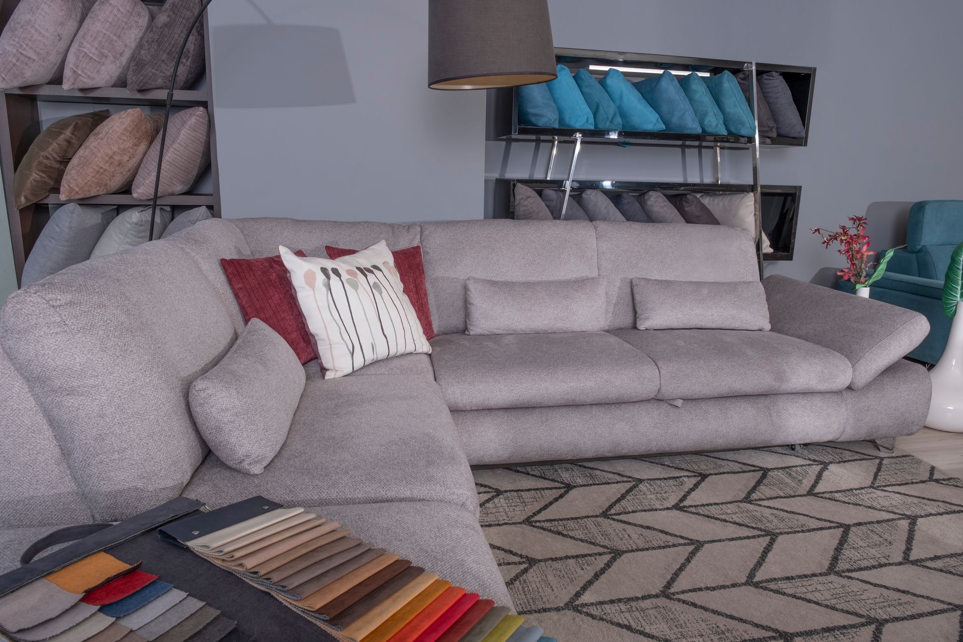 Divano componibile grigio in uno showroom, cuscini, campioni di colore, tappeto a fantasia.