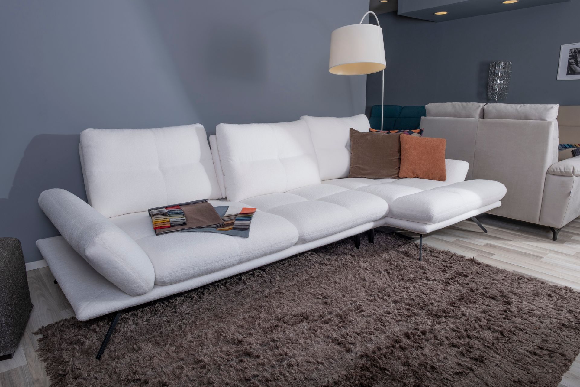 Divano componibile bianco con cuscini e tappeto marroni, sotto una lampada in una stanza con una parete blu.