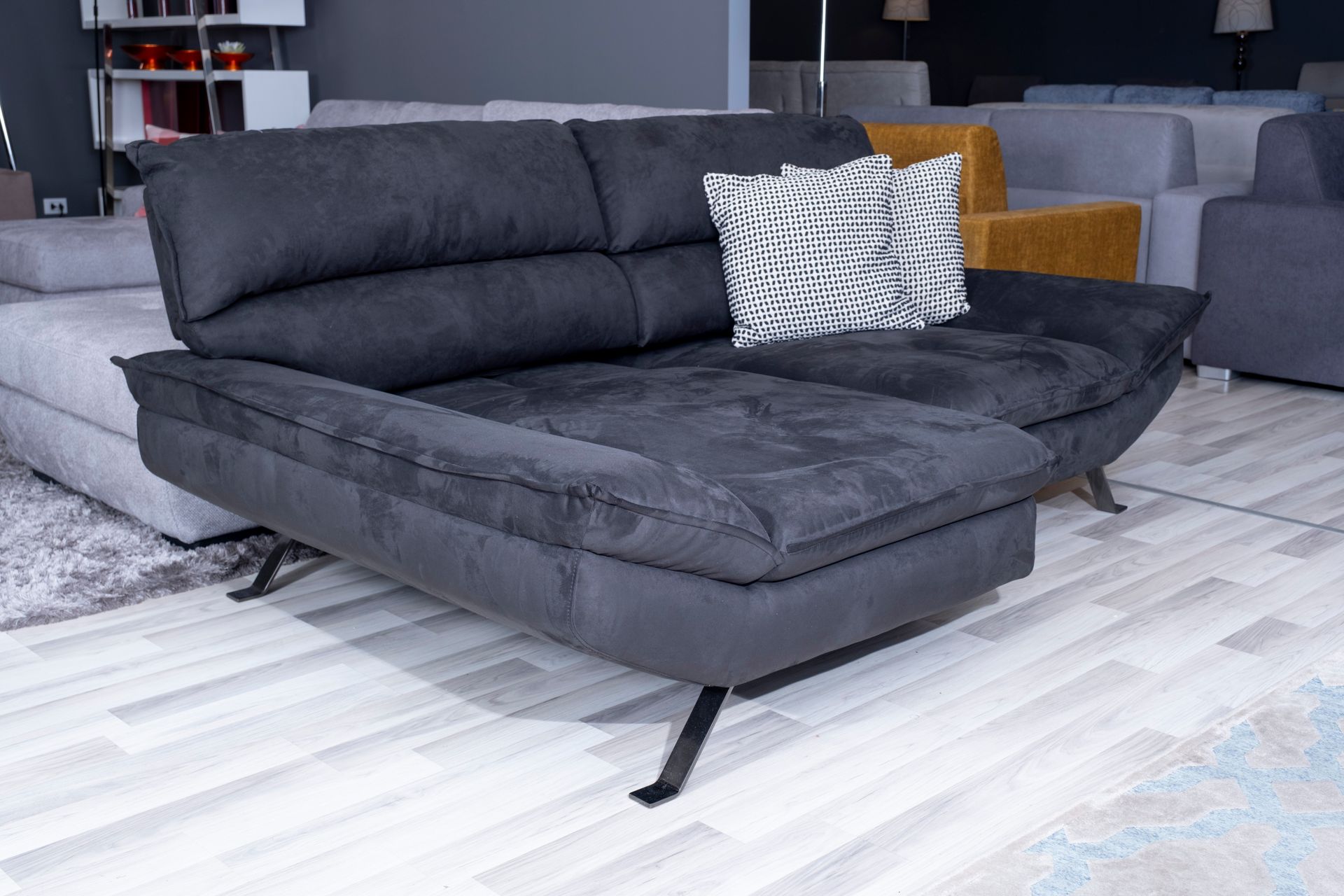 Chaise longue grigio scuro con due cuscini e gambe in metallo. Un cuscino decorato è appoggiato sulla seduta.