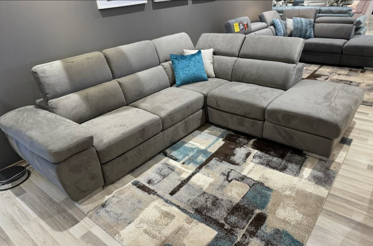 Divano componibile grigio con chaise longue, appoggiato su un tappeto fantasia; cuscino verde acqua.