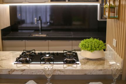 A modern kitchen island with a black stovetop, white stone countertop, and a potted green plant, with a sink area behind.