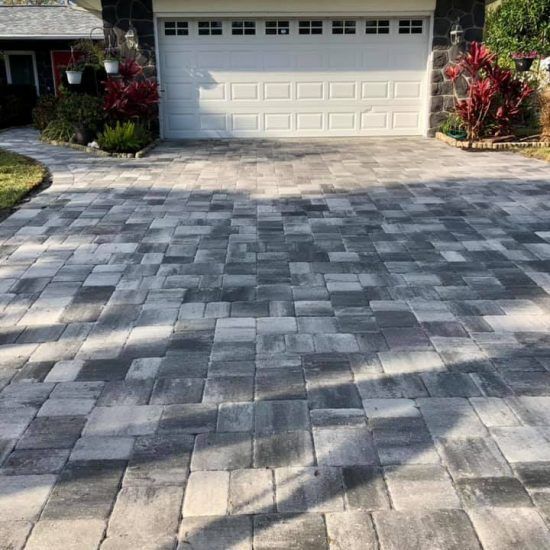 A brick driveway leading to a garage door of a house.