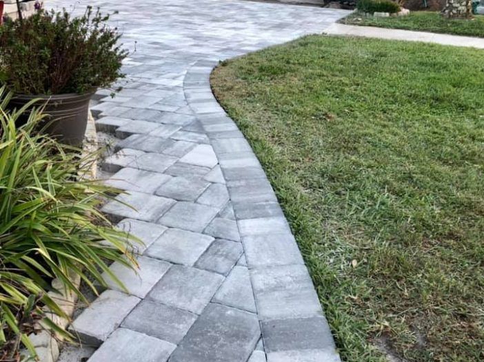 A brick driveway leading to a garage door of a house.