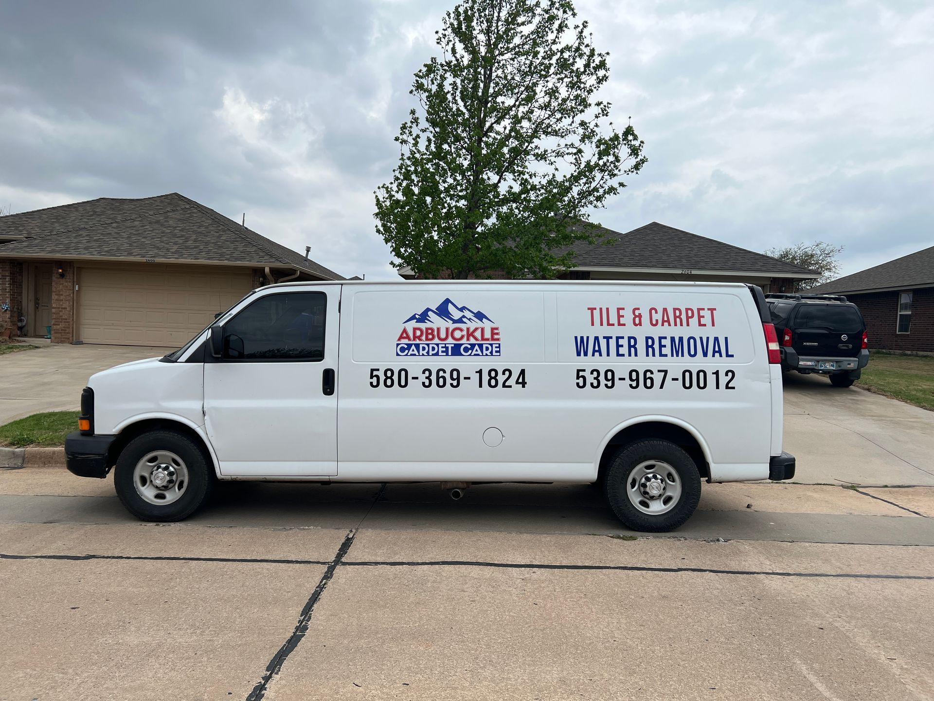 A person wearing orange gloves uses a carpet cleaning machine to vacuum a deep brown, shaggy carpet.